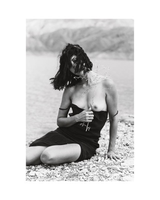 Lusine Davtyan, photographed by Lilit L Hovhanni: sitting on a stony shore, hair blown across her face.