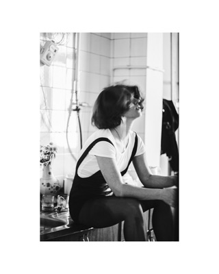 Lusine Baghdasaryan, photographed by Lilit L Hovhanni: seated against a white wall beside a vase and a radio.