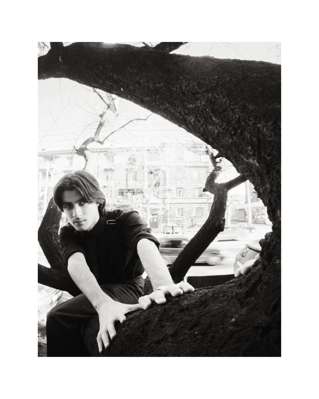 A dark-haired man in dark clothing outdoors, shown in black and white.