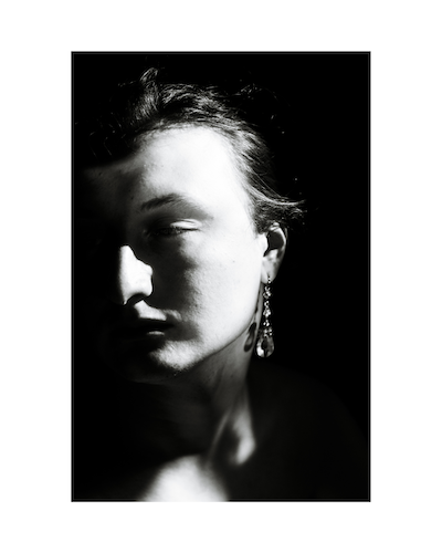 A person fills a vertical black-and-white frame, with bright highlights and deep shadows.