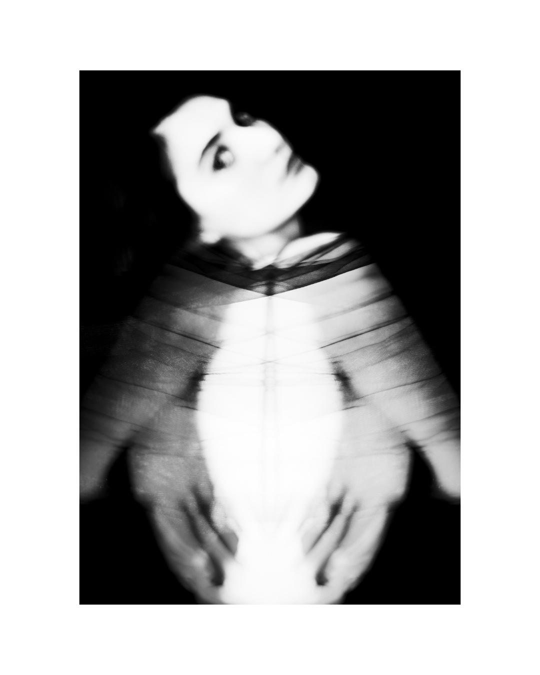 A dark-haired woman faces the camera within a white border, her face and upper body closely framed.
