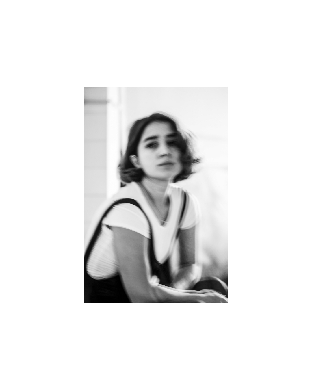 A seated woman in a white T-shirt and dark straps in a black and white portrait by Lilit L Hovhanni.