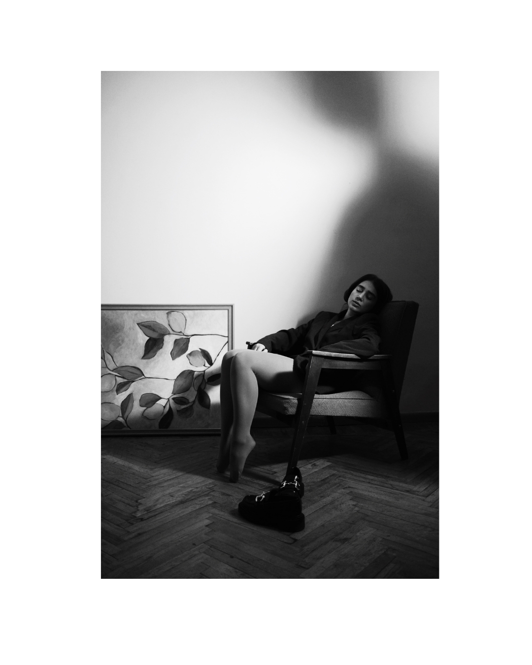 Vertical composition of a woman in dark clothing, surrounded by room furnishings and contrasting light.