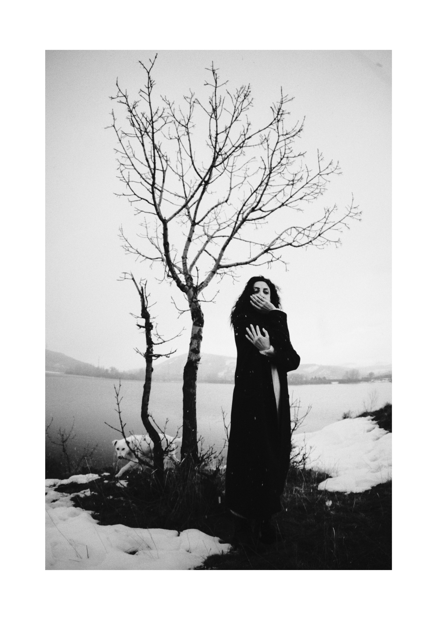 A dark-clad figure outdoors on patchy snow, shown in black and white.