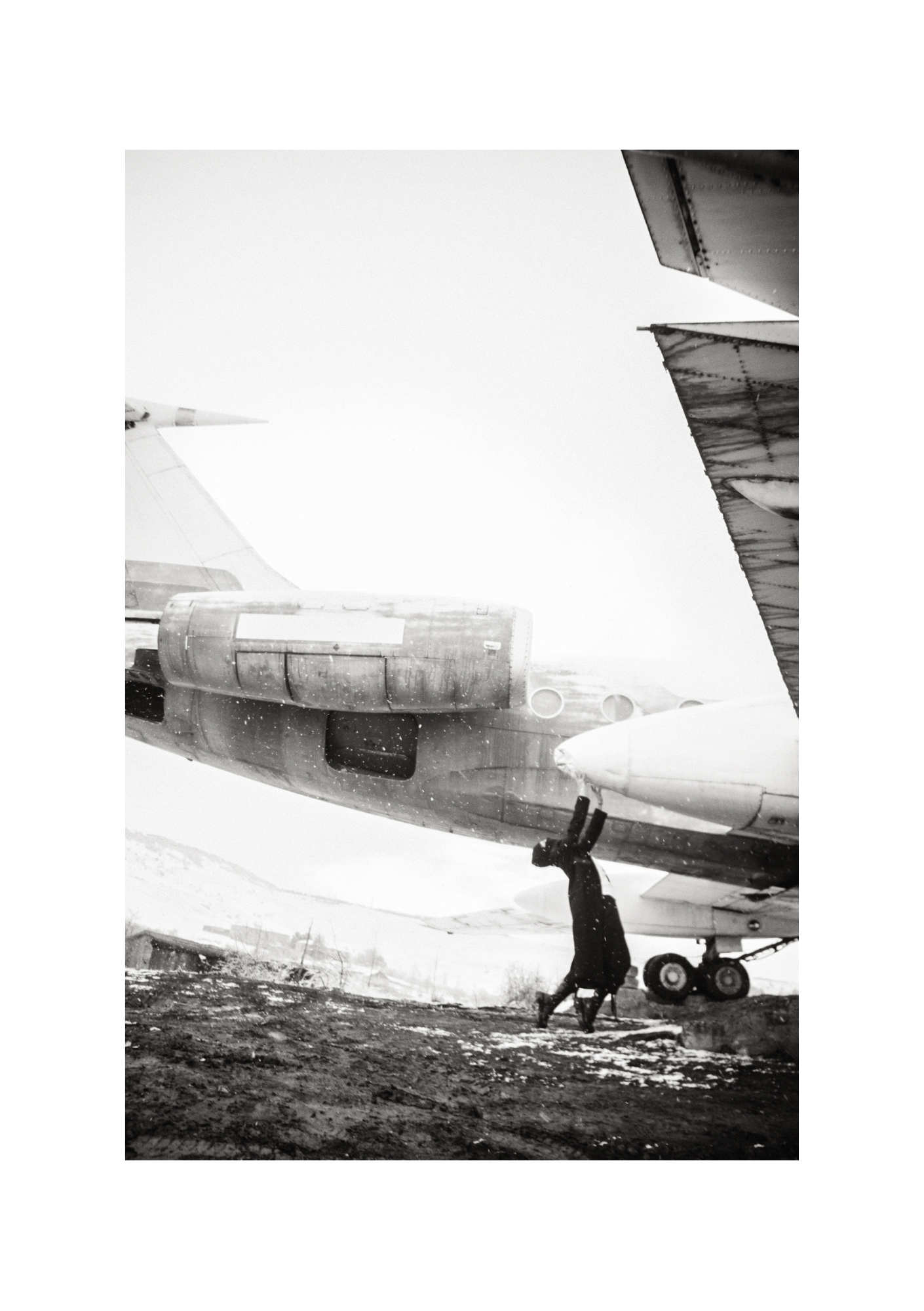 A dark-clad figure outdoors on patchy snow, shown in black and white.