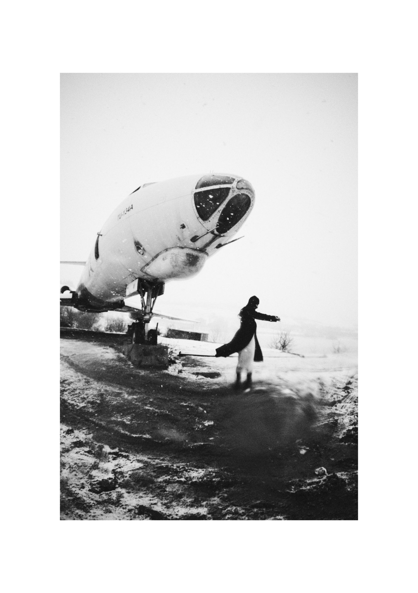 A figure in dark clothing against a pale, snow-dusted landscape, with the full body in view.