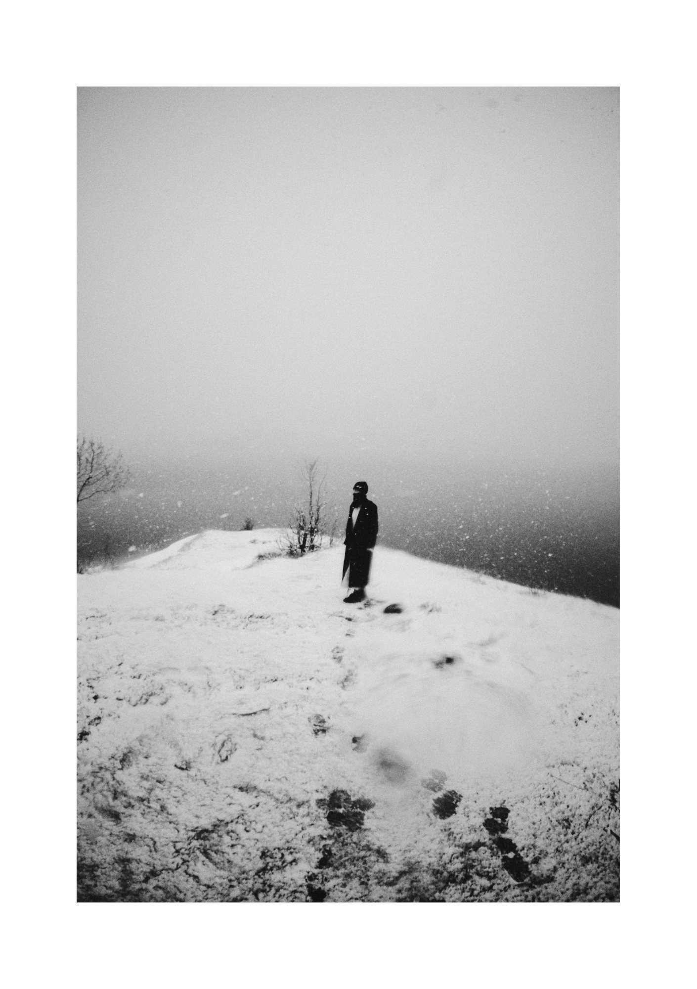 A dark-clad figure outdoors on patchy snow, shown in black and white.
