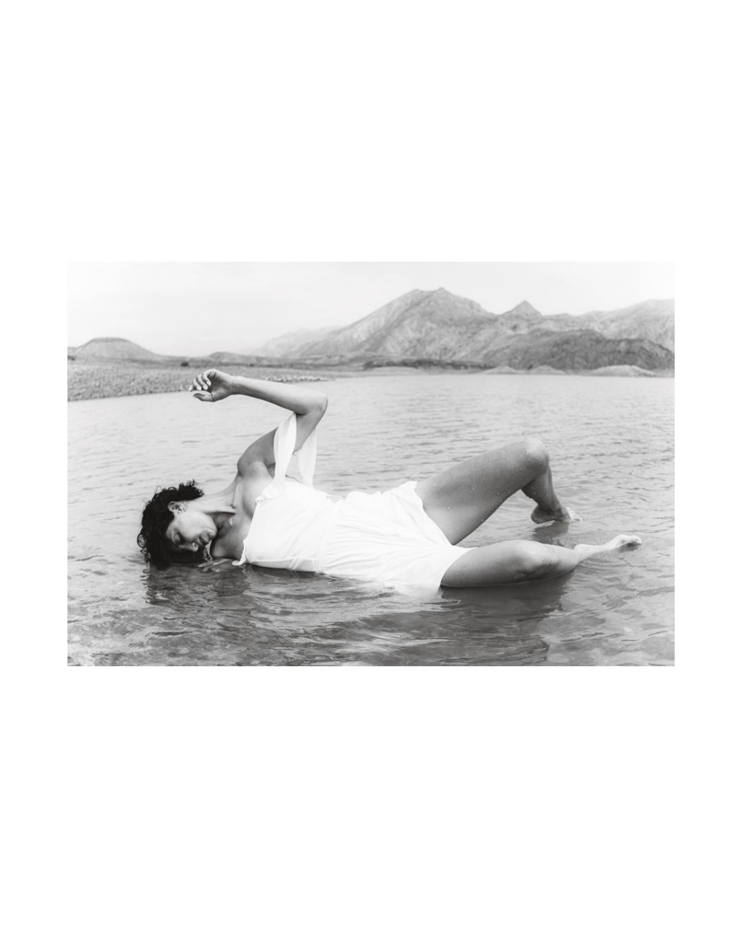 Black-and-white view of a woman in draped clothing, surrounded by water and rock.