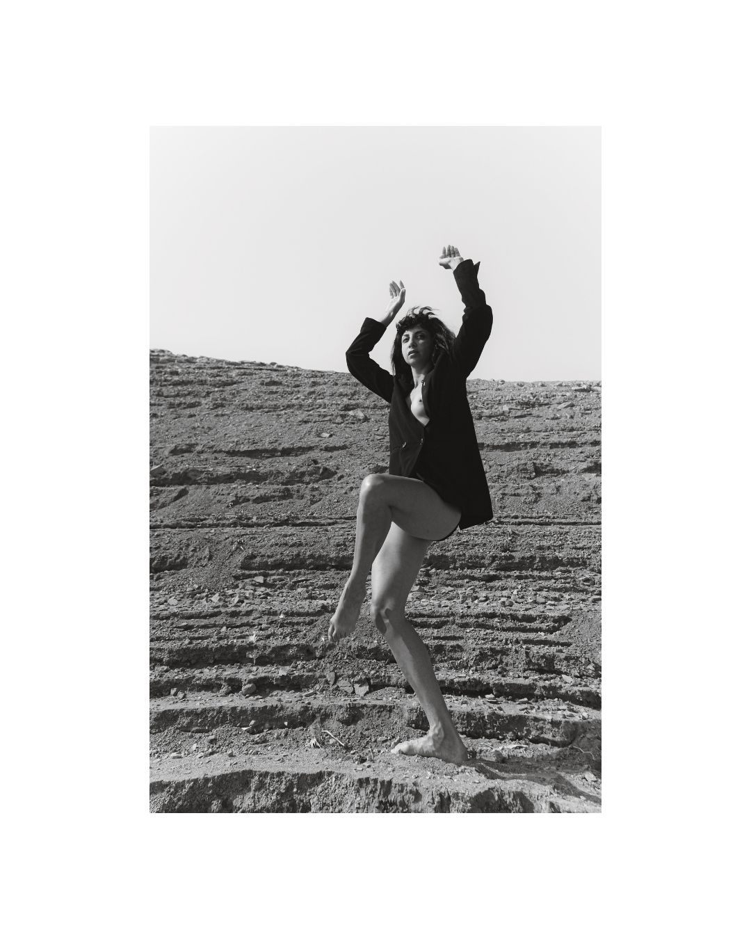 A woman poses in a rocky waterside landscape, in black and white.