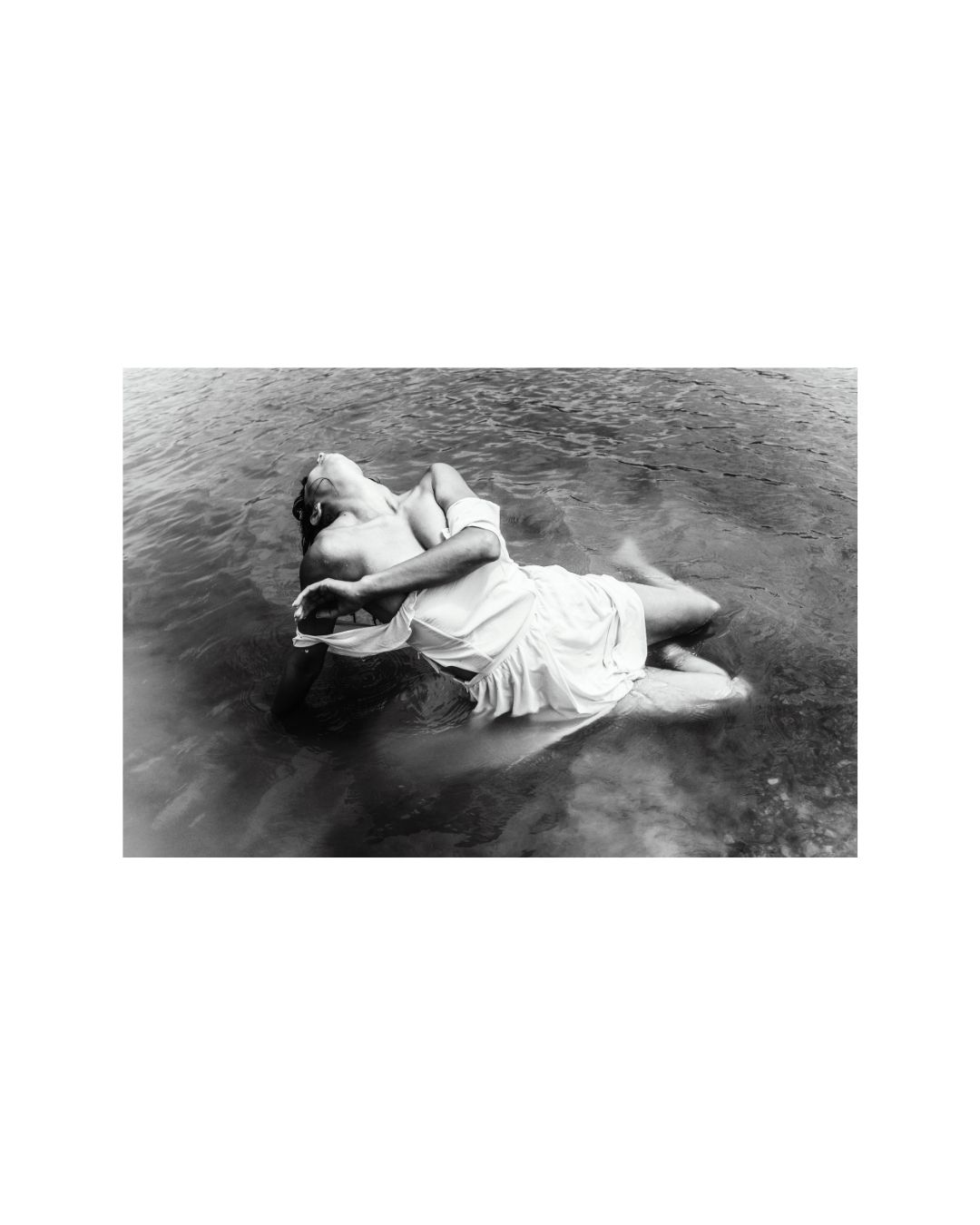 Black-and-white view of a woman in draped clothing, surrounded by water and rock.