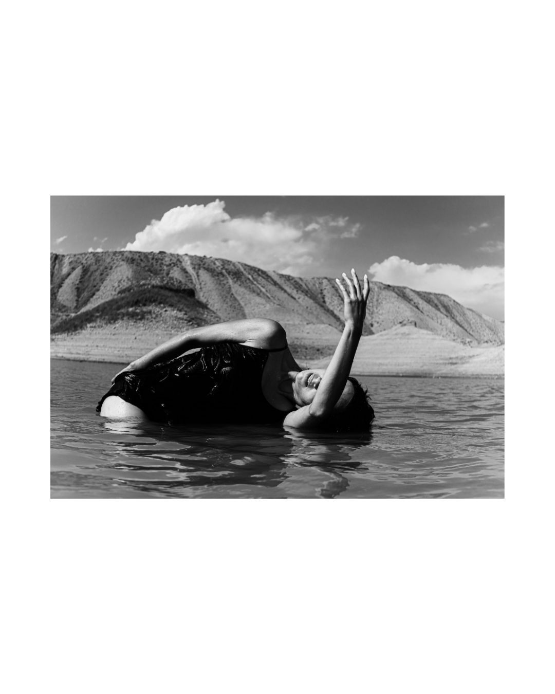 A woman poses in a rocky waterside landscape, in black and white.
