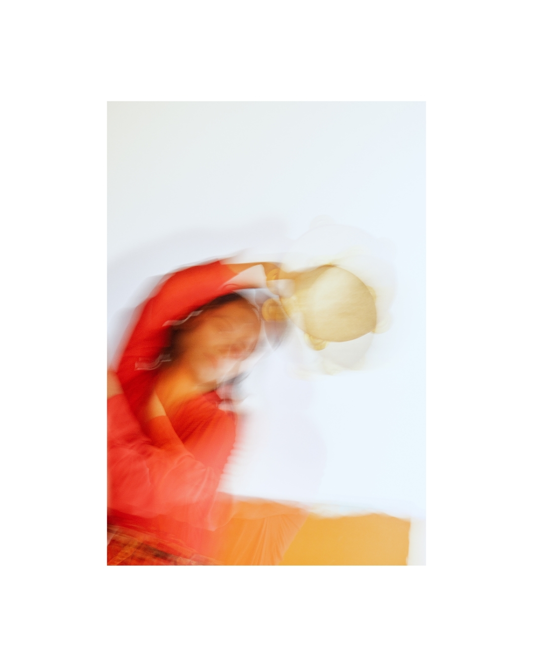 A woman in red-orange clothing appears in soft focus in a bright room with pale walls.