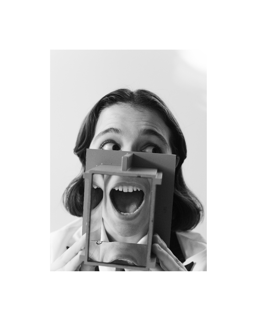 A dark-haired person in a light shirt holds a frame over parts of the face, shown in black and white.
