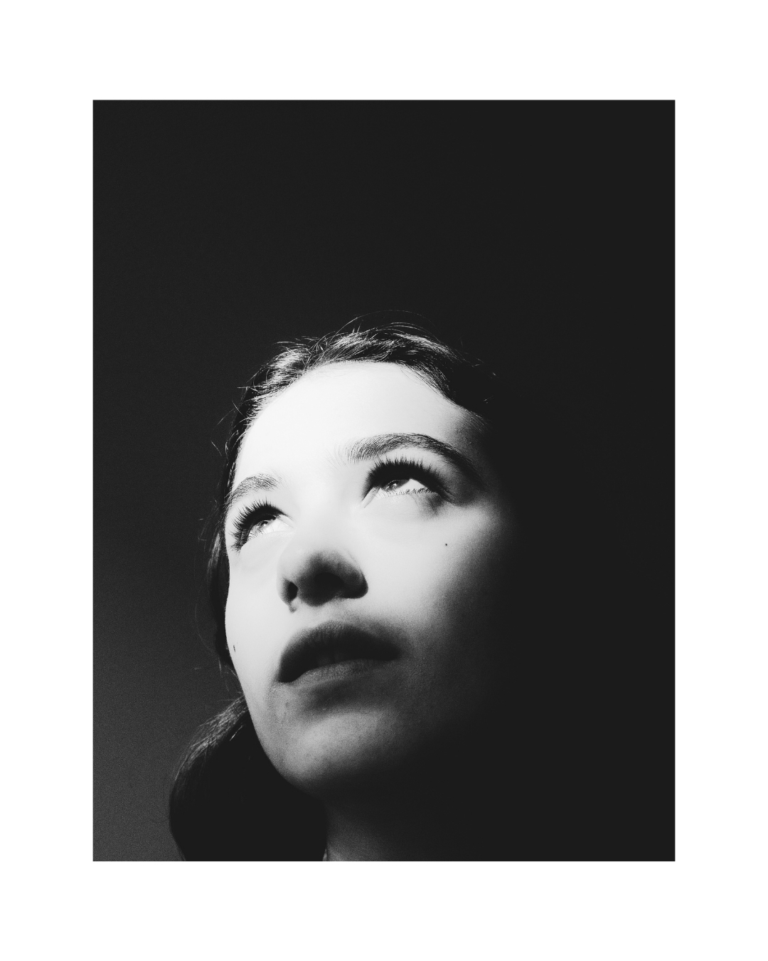 A woman with short dark hair indoors, her face lit against areas of shadow, in black and white.