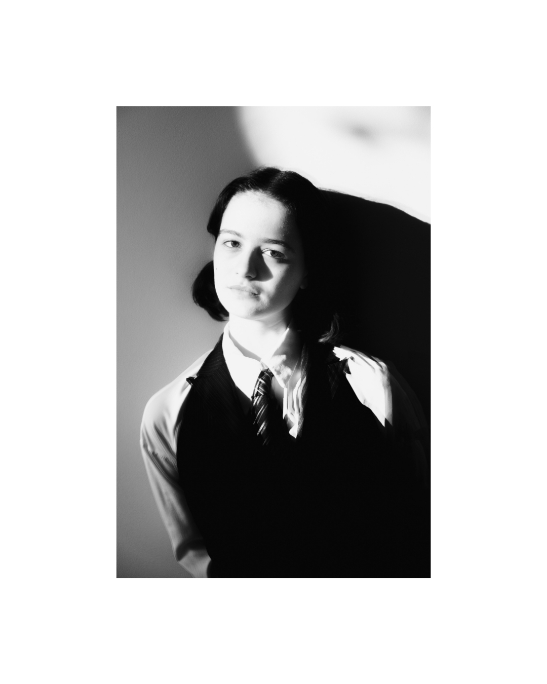A dark-haired woman indoors, shown in black and white within a tall frame and broad white border.