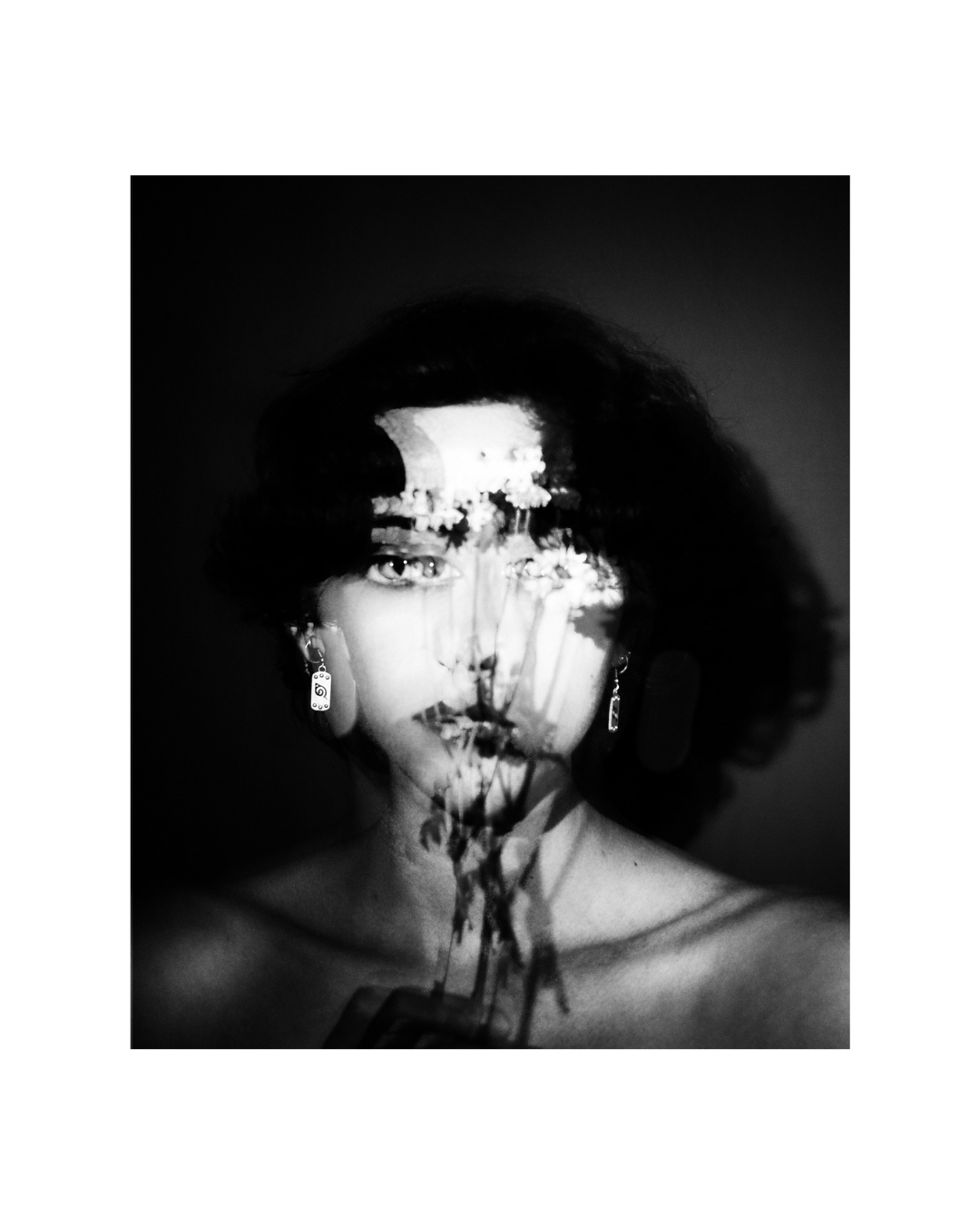 A short-haired woman in black and white, her face partly obscured by overlapping light and dark shapes.