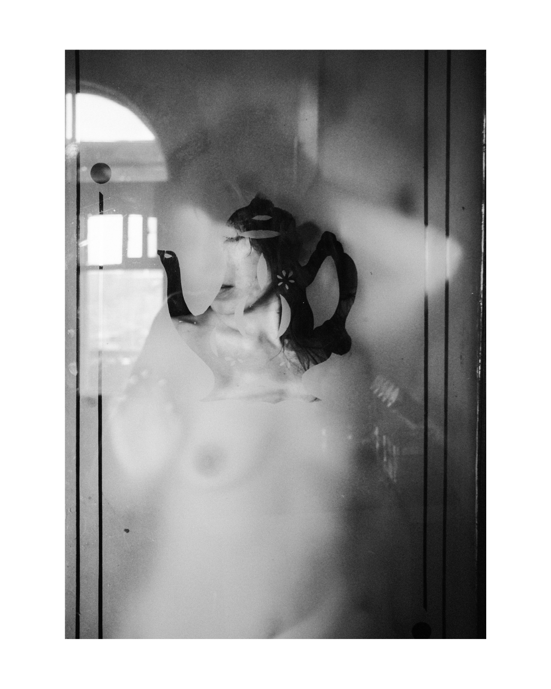 A woman's face partly obscured by frosted glass and a teapot motif, with window reflections in black and white.