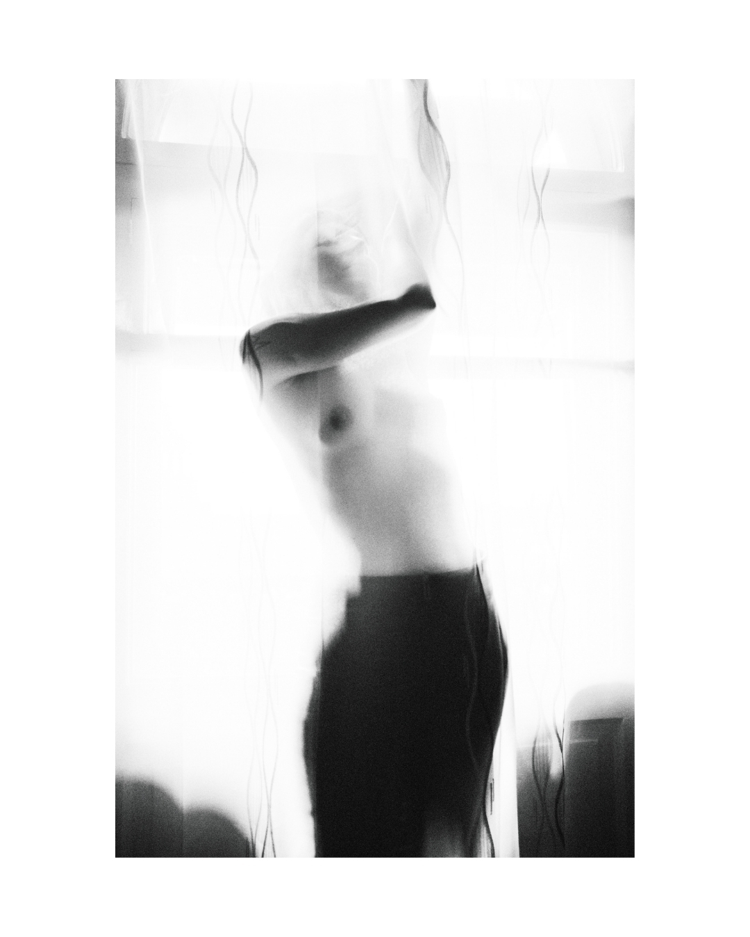 A blurred figure behind translucent patterned fabric, shown in black and white with bright light around the body.