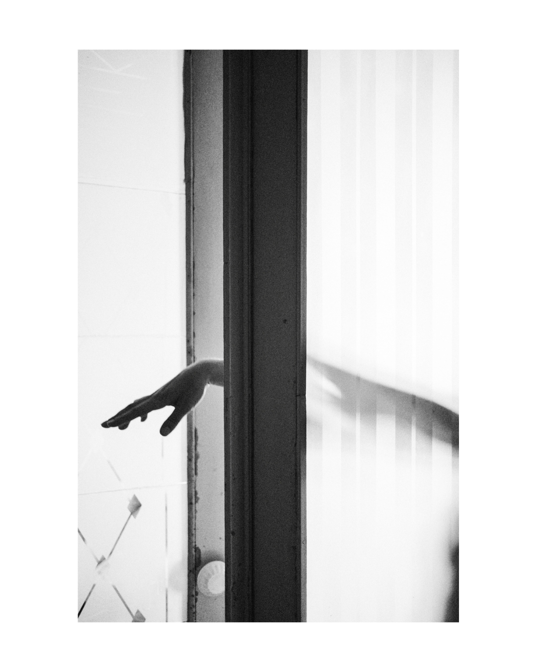 Black and white view of a figure behind patterned material, with softened outlines and a wide white border.