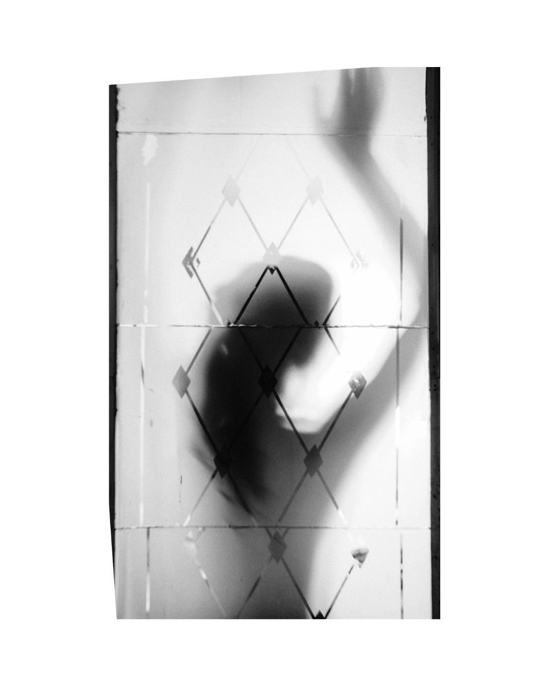 Black and white view of a figure behind patterned material, with softened outlines and a wide white border.