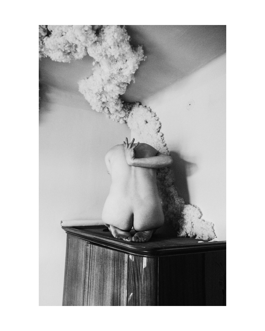 A seated figure in black and white, with the body and surroundings divided by light and shadow.