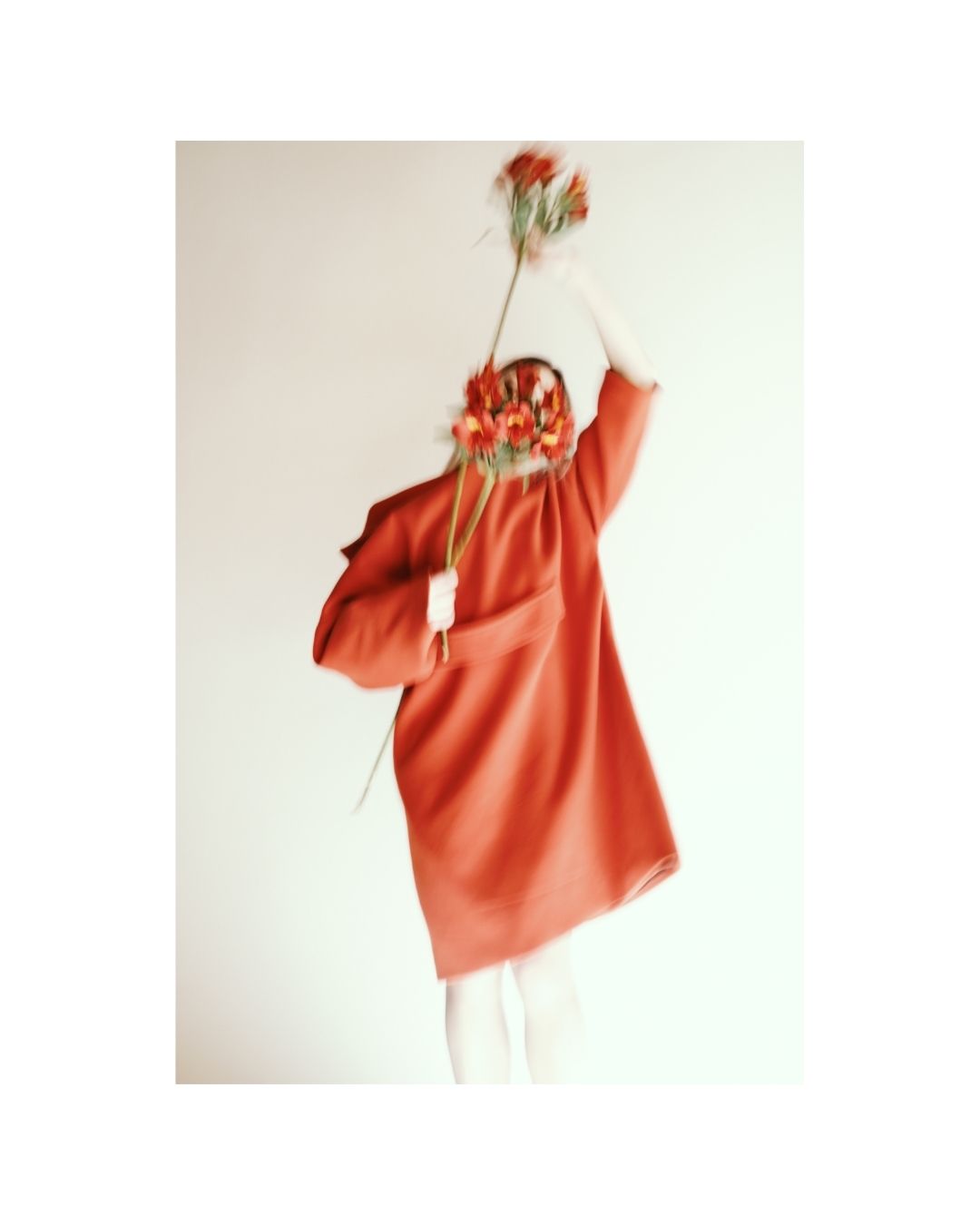A person wearing a loose red coat in a bright interior with soft, diffused light.