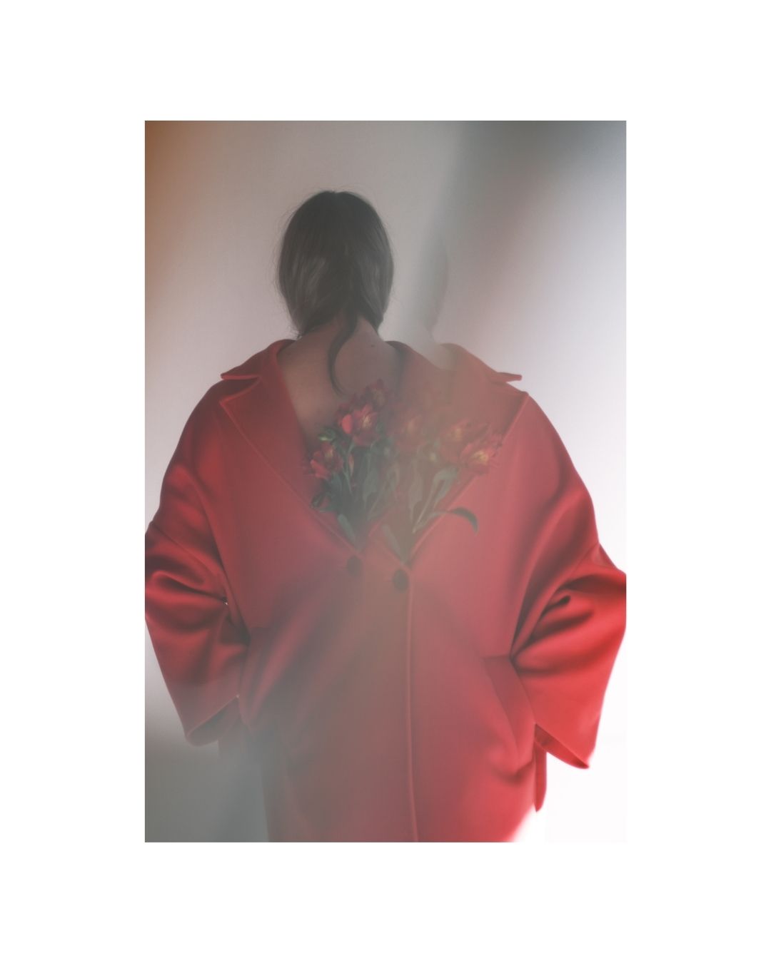 A person wearing a loose red coat in a bright interior with soft, diffused light.