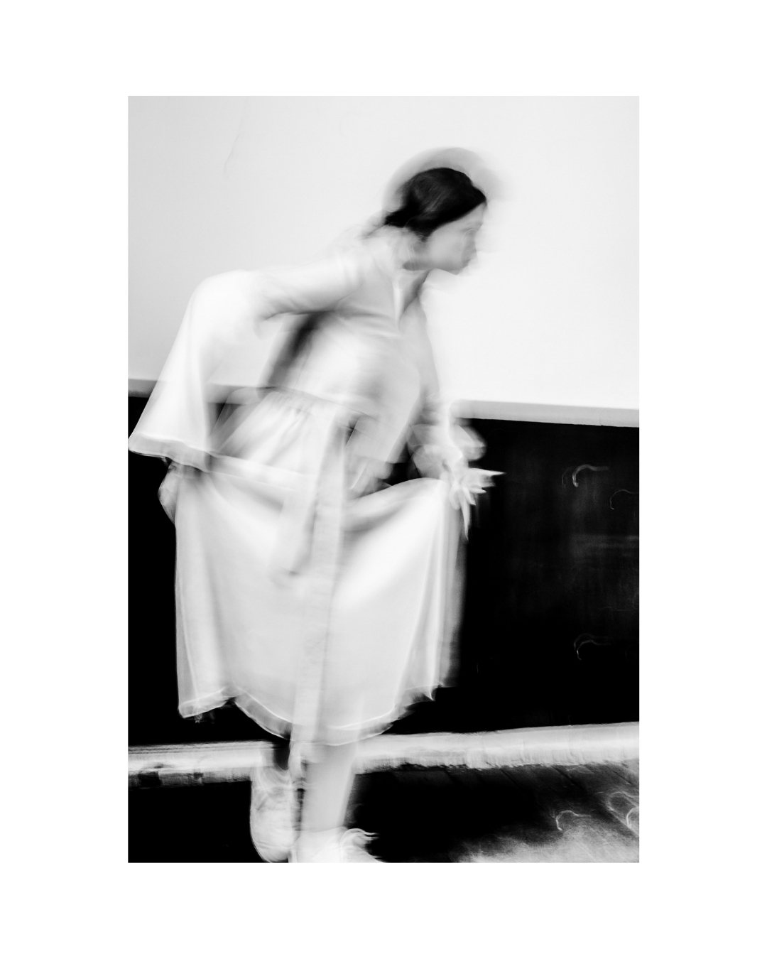 Black-and-white composition of pale clothing against a dark wall, surrounded by a wide white border.