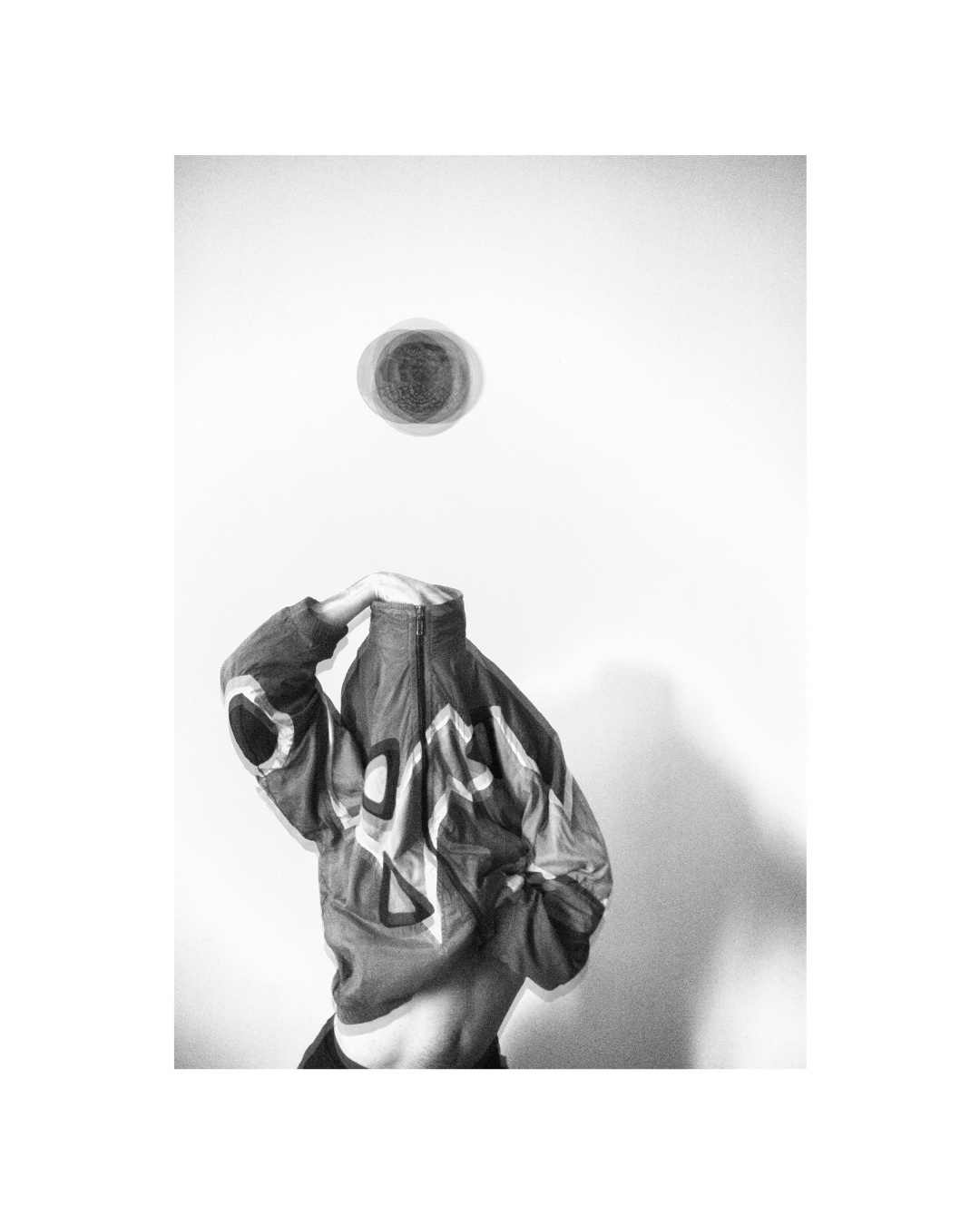 Black-and-white figure with the face obscured, set within a vertical frame and broad white margins.