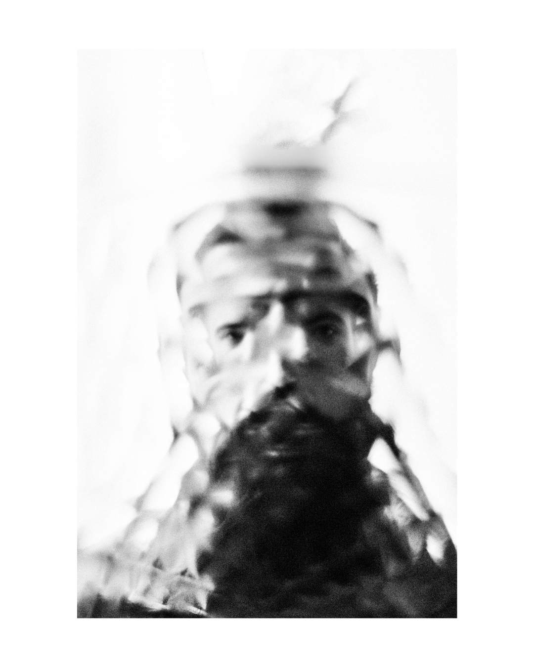 A figure with an obscured face against a pale background, in black and white.