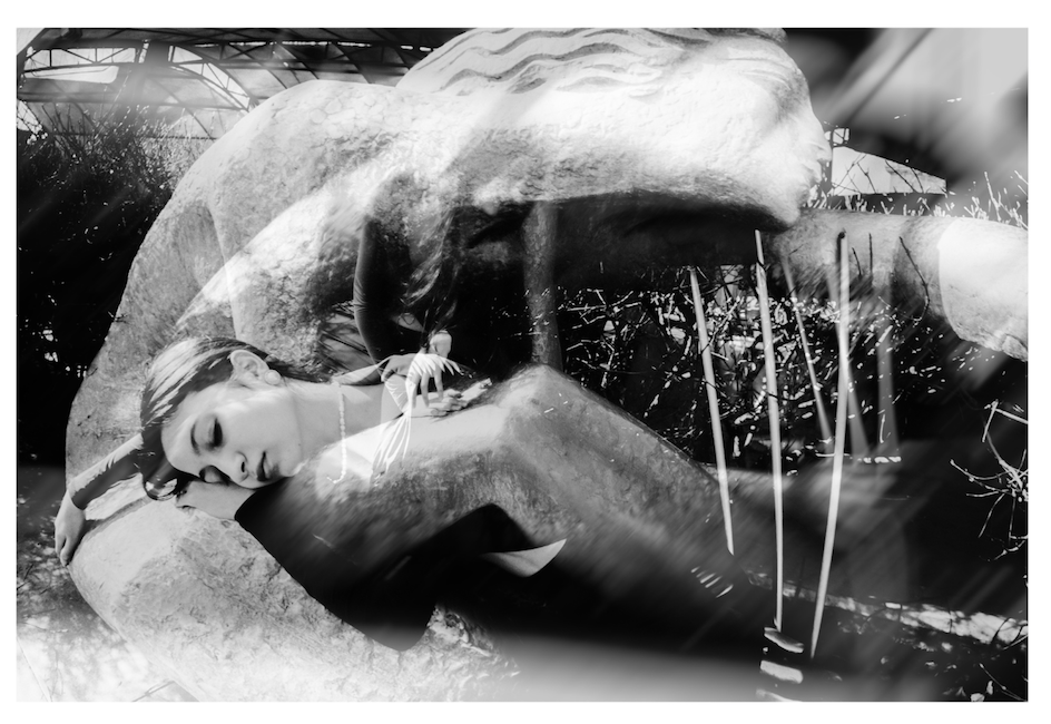 A reflection doubles a monument and the woman standing near it, in black and white.