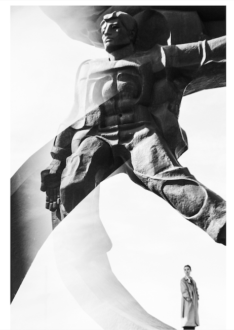 A reflection doubles a monument and the woman standing near it, in black and white.