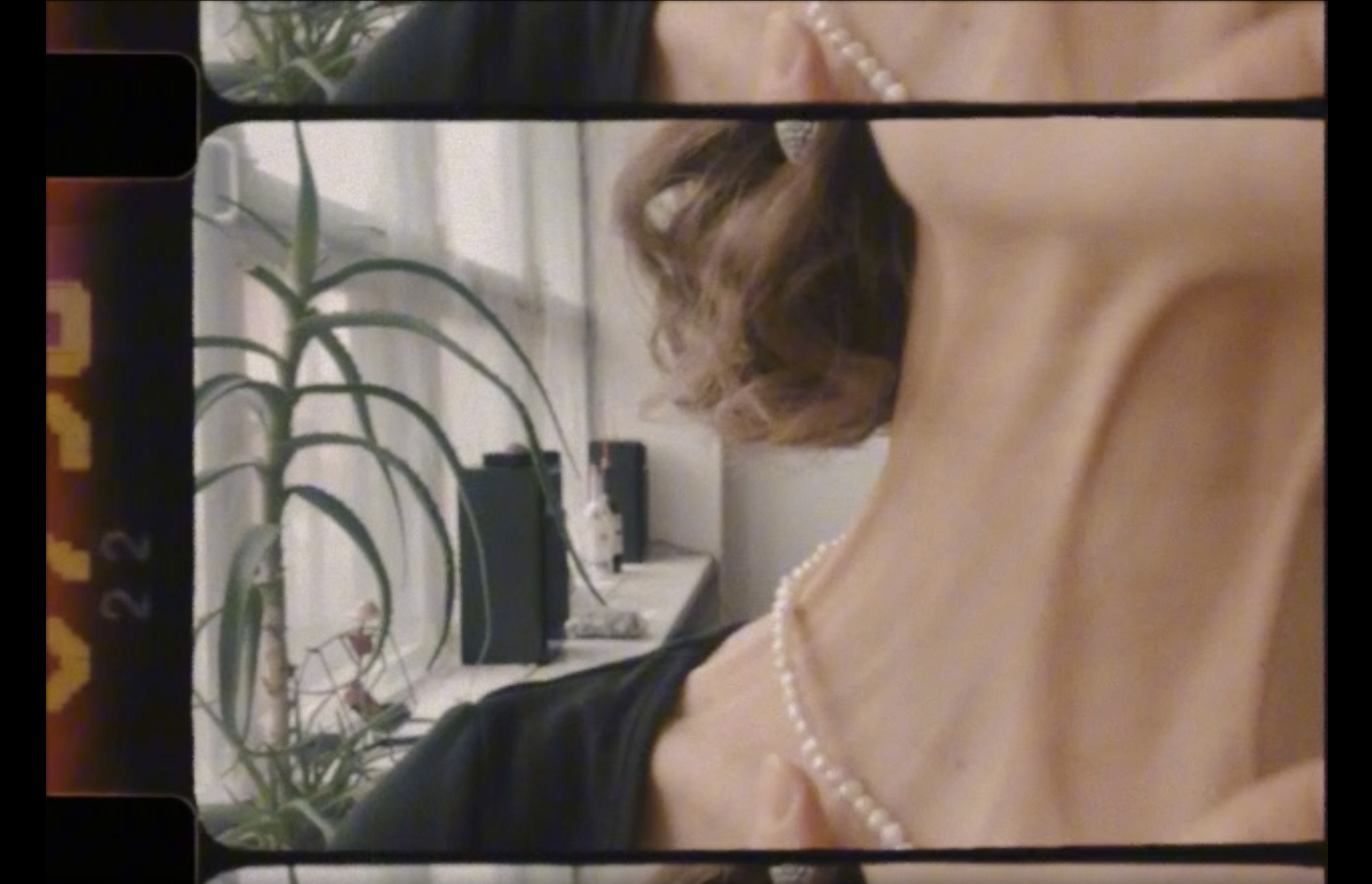 A frame from The Neck: a neck and jaw with a pearl necklace, turned on its side in a film strip, a plant by the window.